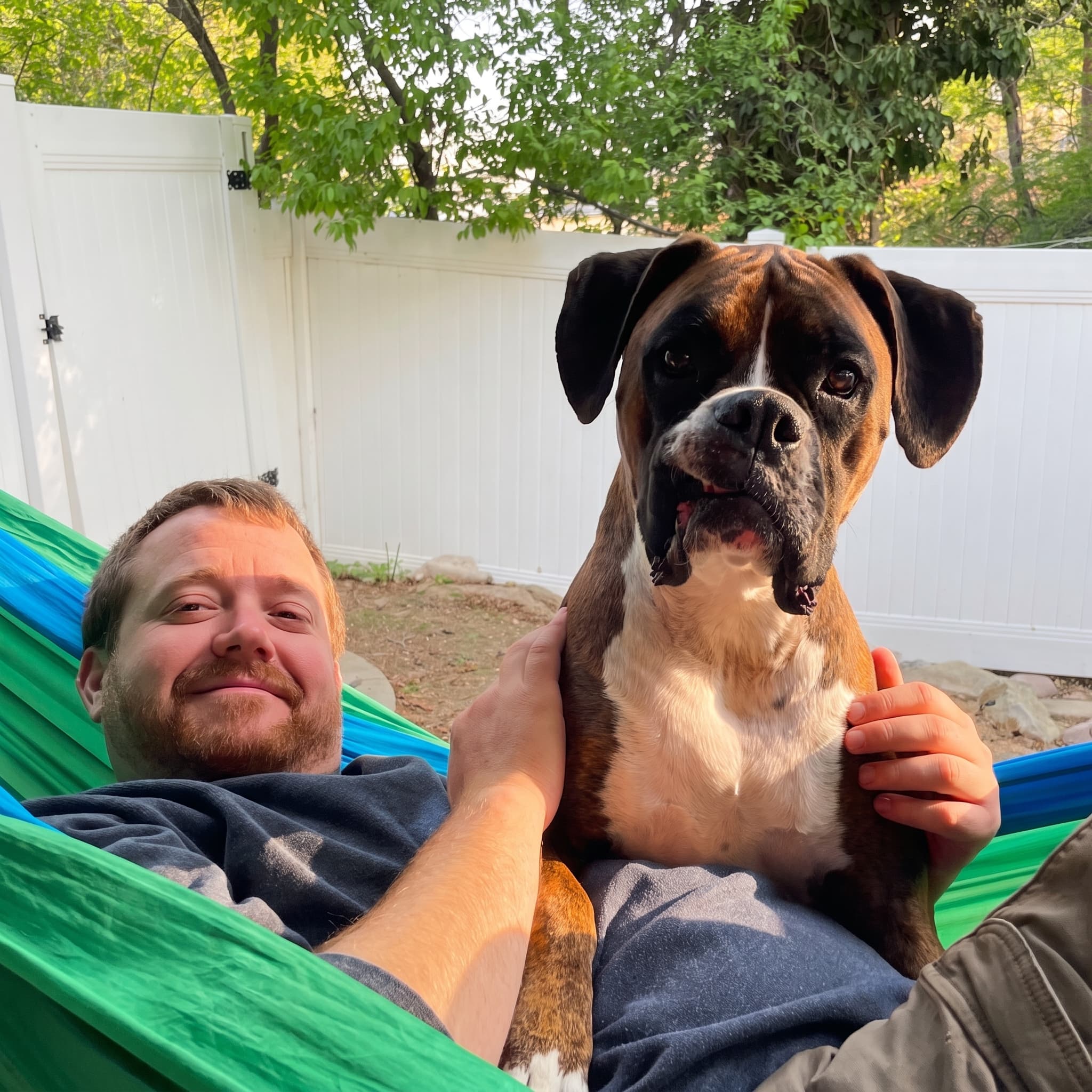 Matt relaxing in a backyard hammock with a boxer dog